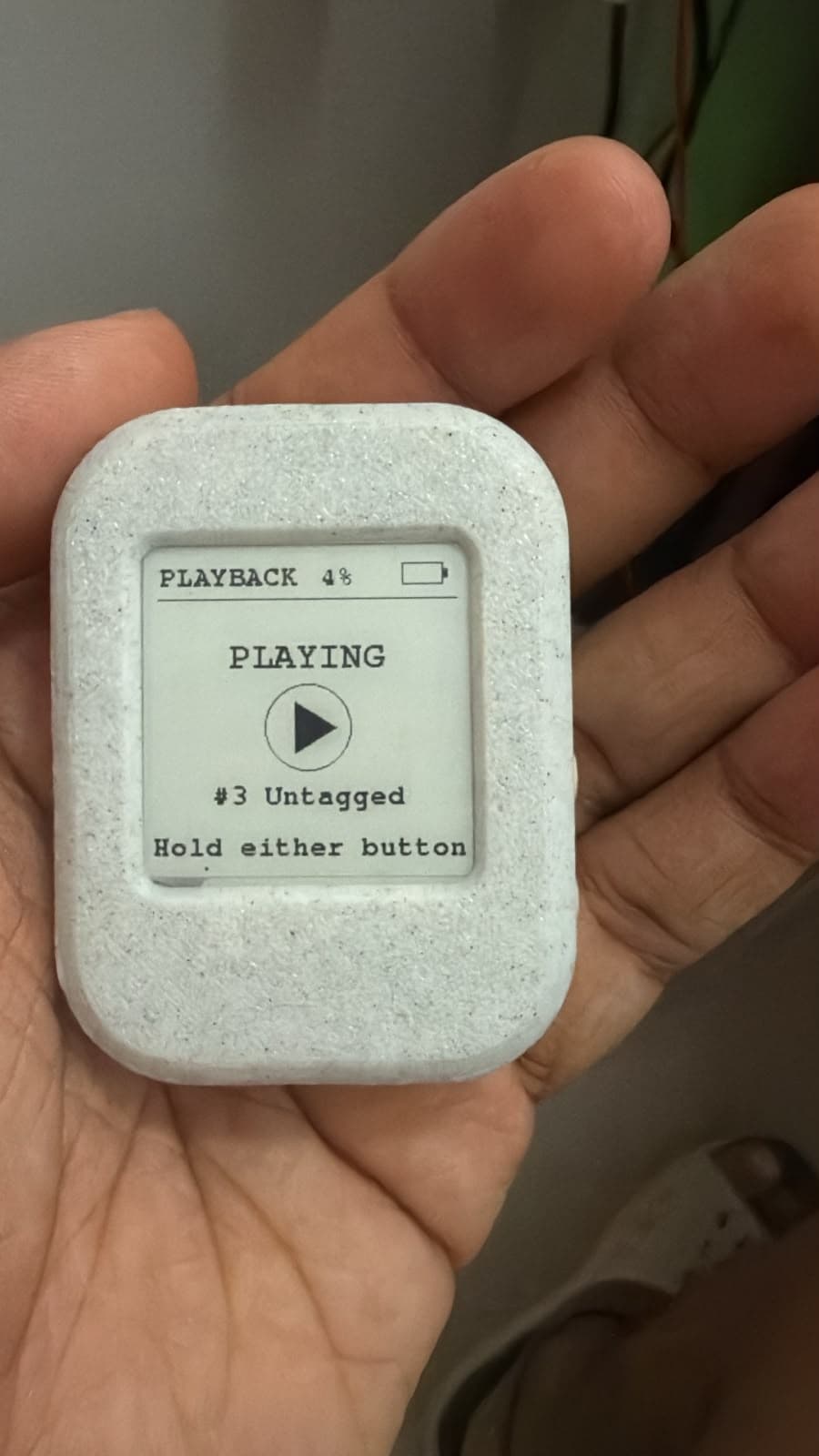 Early Aira hardware prototype held in a hand with its e-paper screen showing playback