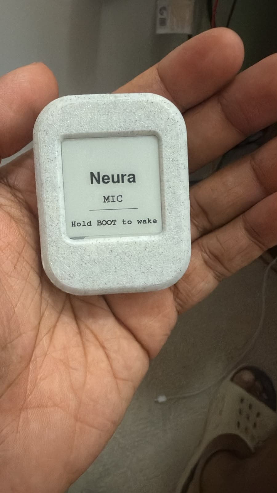 Early Aira hardware prototype held in a hand with its temporary Neura name on the e-paper screen